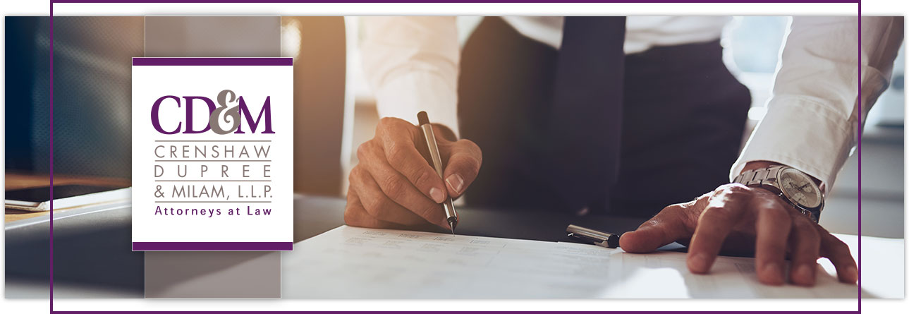 Lawyer filling out paperwork on a table, overlaying Crenshaw Dupree & Milam Logo